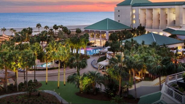 Ein Resort mit Pool, Palmen und Blick auf das Meer bei Sonnenuntergang.