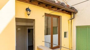 Un bâtiment jaune avec un balcon en bois, une porte et une fenêtre avec des volets verts.
