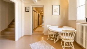 Une pièce avec une table à manger blanche, des chaises blanches, un radiateur blanc et un escalier.