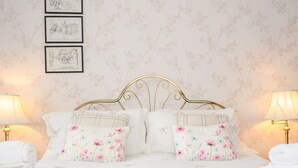 Una cama bien arreglada con almohadones florales, un cabecero dorado y dos lámparas de noche.