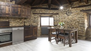 Una cocina rústica con paredes de piedra, armarios de madera, una mesa de comedor y un reloj.