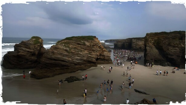 Una playa rocosa con grandes rocas y una multitud de gente.