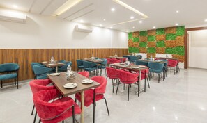 A modern dining area with wooden paneling, teal and red chairs, and a green and brown decorative wall. - Treebo Gatiman (Dera Bassi)