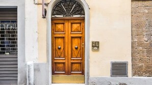 Une porte à deux battants en bois, surmontée d’une arche métallique, est encastrée dans un mur de couleur beige, avec une section en pierre sur le côté droit.