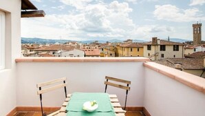 Un balcon avec une table et des chaises, donnant sur un paysage urbain avec des immeubles et une tour.