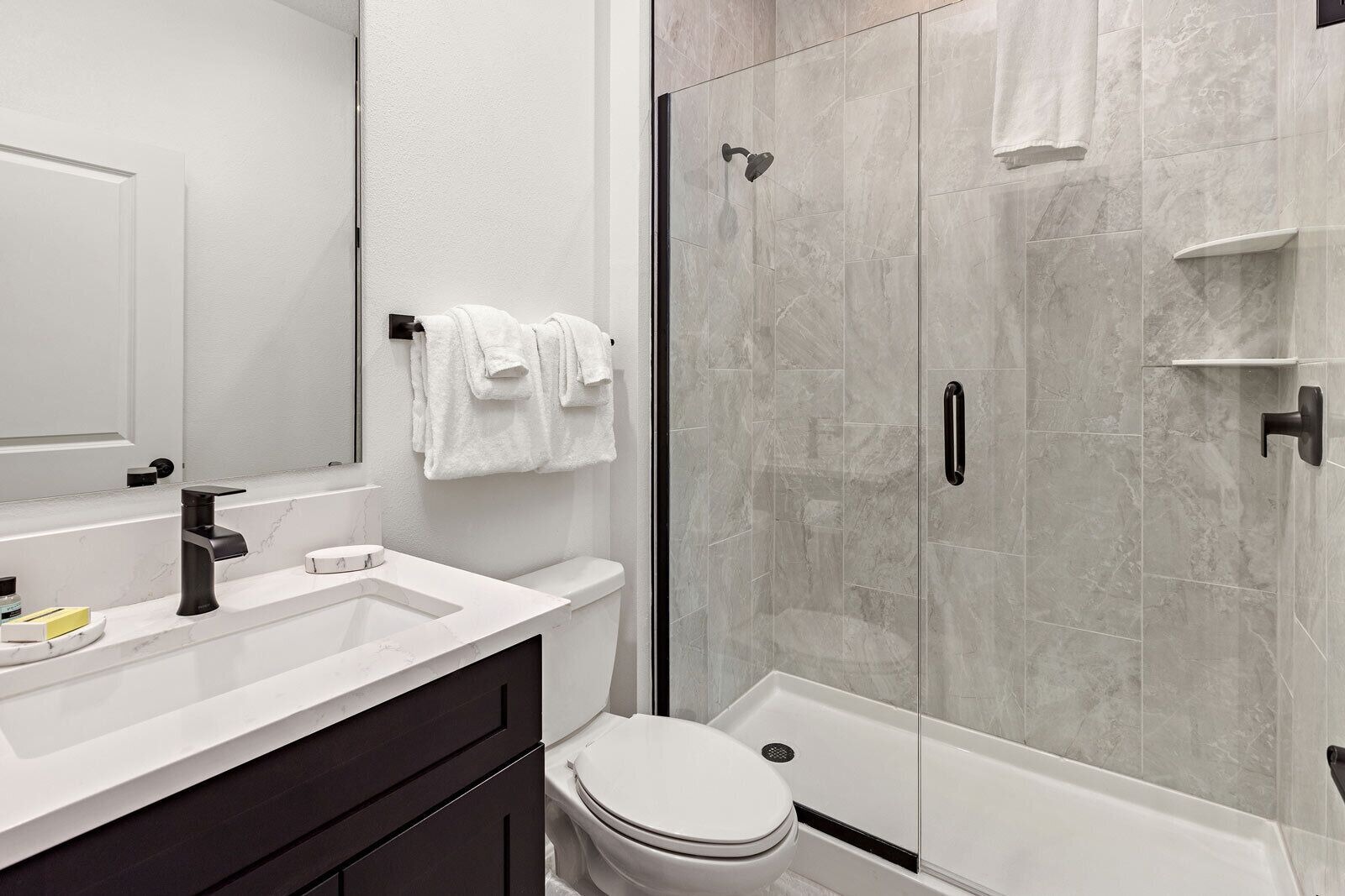 A modern bathroom with a white sink, black faucet, and a glass-enclosed shower.