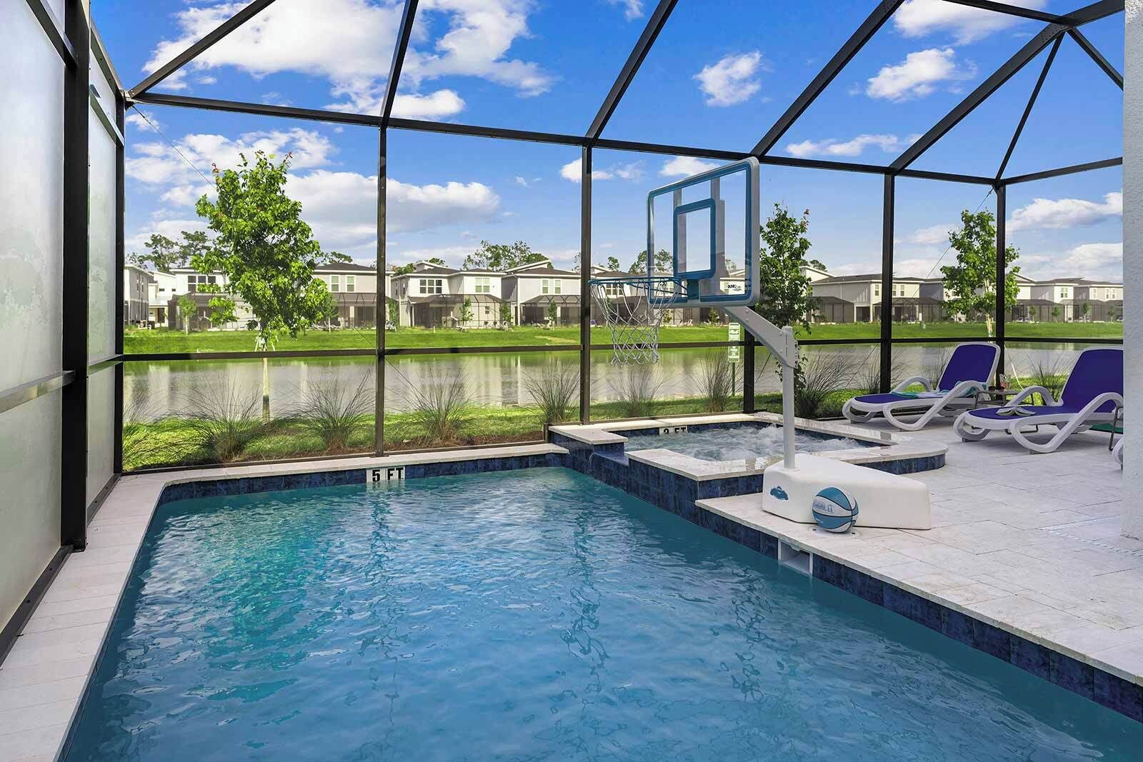 Une piscine avec vue sur un quartier résidentiel, un panier de basketball et des chaises longues.