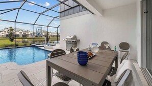 Un patio con piscina, una parrilla y una mesa con sillas.