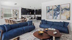 A modern living room with two blue sofas, a coffee table, and a dining area with a white table and chairs.