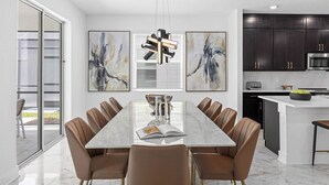 A modern dining room with a marble table and leather chairs, a kitchen with dark cabinets, and abstract art on the walls.
