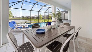 Un espace extérieur abrité, aménagé pour les repas, avec une piscine, des chaises longues et un barbecue.