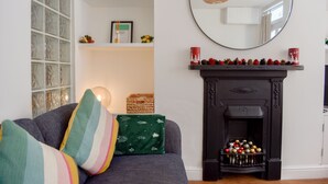 En stue med pejs, en sofa med stribede puder, et spejl og en reol med dekorative genstande.