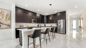 A modern kitchen with dark cabinets, stainless steel appliances, and a marble floor.