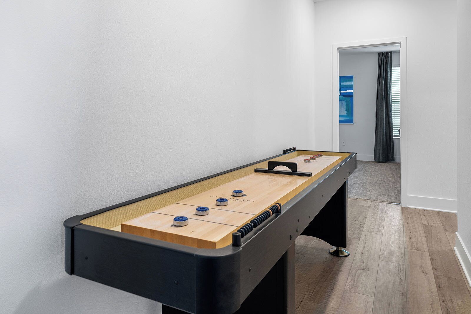 A foosball table in a hallway with a view of a room through an open door.