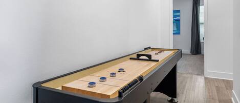 A foosball table in a hallway with a view of a room through an open door.
