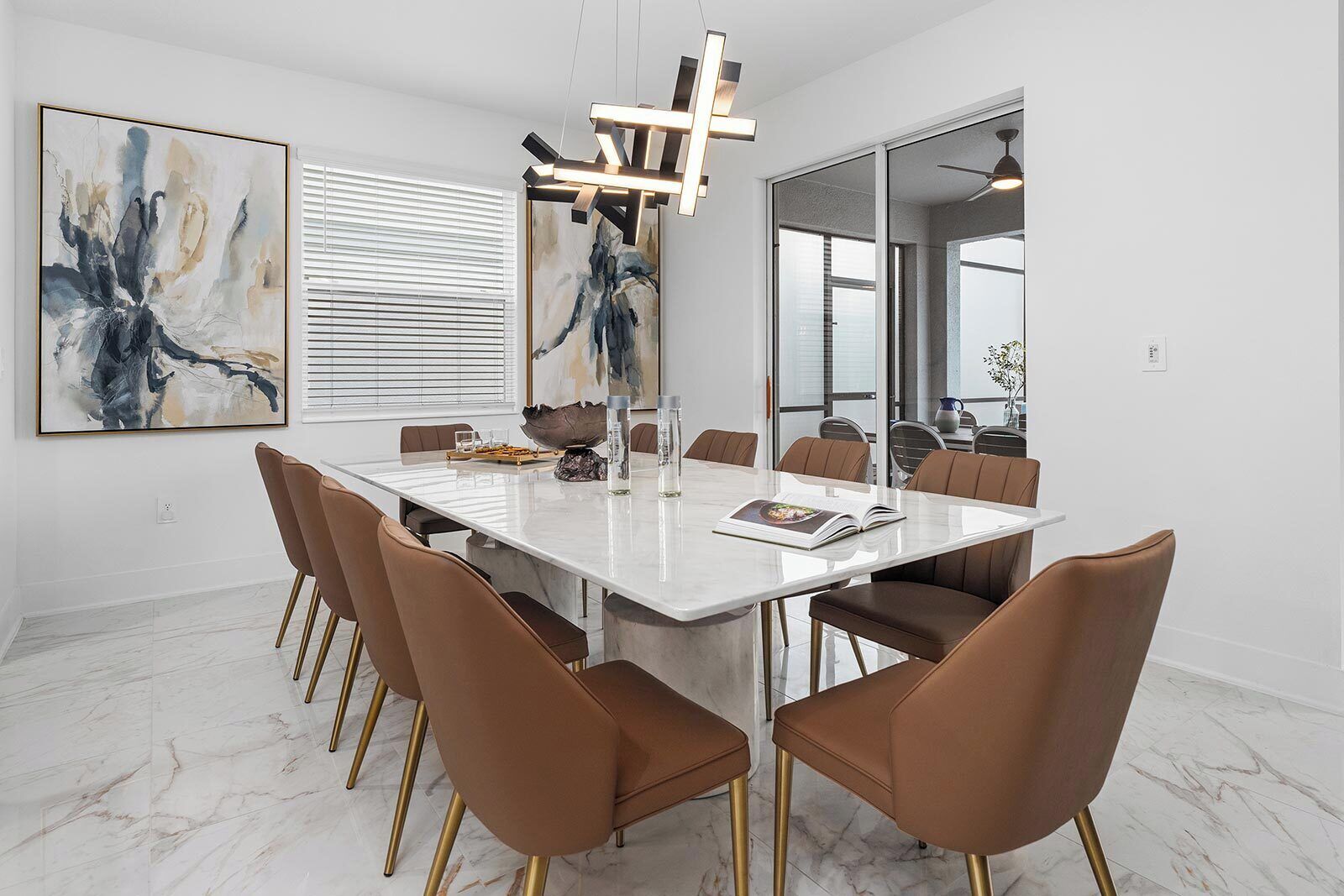 Un comedor moderno con suelo de mármol, una mesa blanca y sillas marrones con patas doradas.