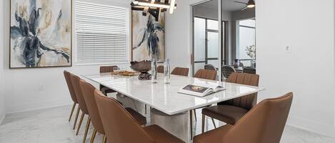 Un comedor moderno con suelo de mármol, una mesa blanca y sillas marrones con patas doradas.