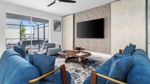 Ein modernes Wohnzimmer mit einem großen Fernseher, blauen Sofas und einem Deckenventilator.