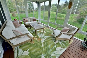 A sunroom with a view of a grassy yard, furnished with a sofa, chairs, and a coffee table. - Bear Trap Dunes Resort Bethany Beach 4BR, 3.5 Bath (Ocean View)