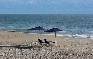 A beach with two umbrellas, a chair, and a small table. - Bear Trap Dunes Resort Bethany Beach 4BR, 3.5 Bath (Ocean View)