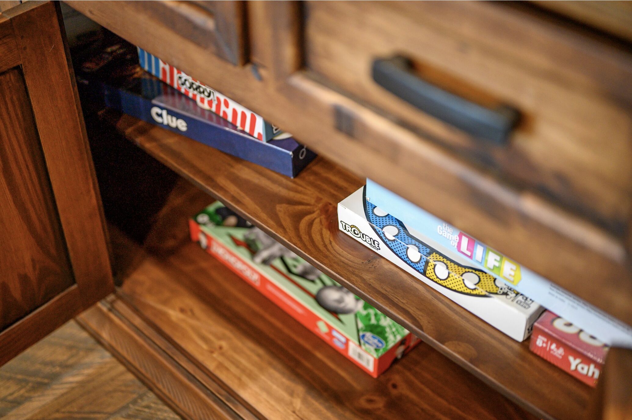 Un calaix de fusta ple de jocs de taula, com ara 'Clue' i 'The Game of Life'.