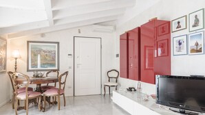 Ein Essbereich mit einem Holztisch und Stühlen, einem Bild an der Wand und einem Fernseher auf einem weißen Schrank.