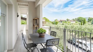 Ein Balkon mit Tisch und Stühlen, einem Blumentopf und Blick auf eine Straße sowie Grünflächen.