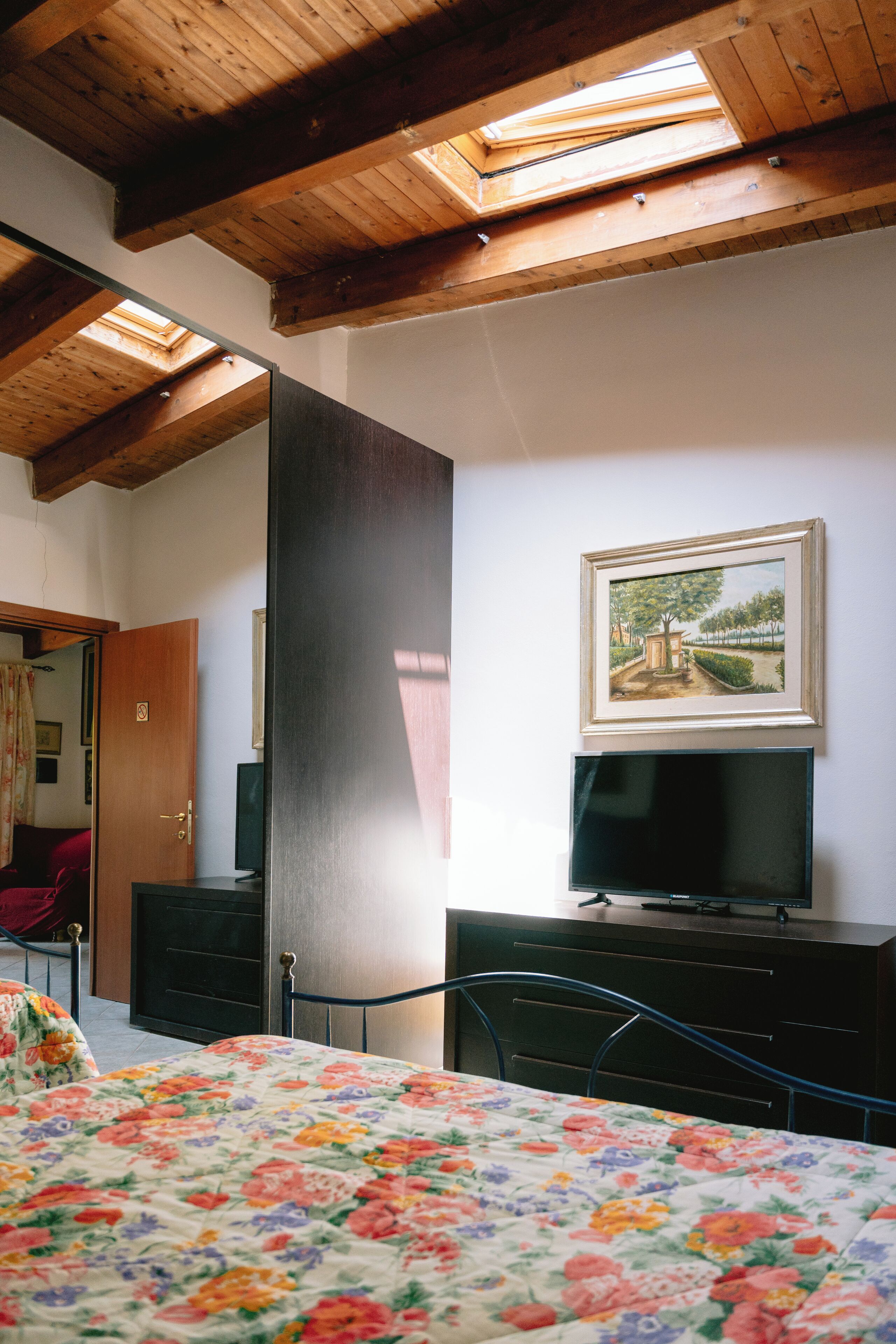 A bedroom with a bed, a TV, a desk, and a painting on the wall.