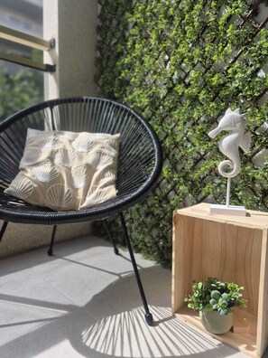 Una silla con cojín, una mesita de madera con una planta, y un adorno de caballito de mar en la pared.