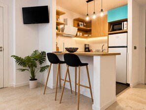 A compact kitchen with a TV, wooden shelves, a microwave, and two bar stools. - PLATAN ApartHotel - Family sized condo with pool, 2 min from the beach! (Salou)
