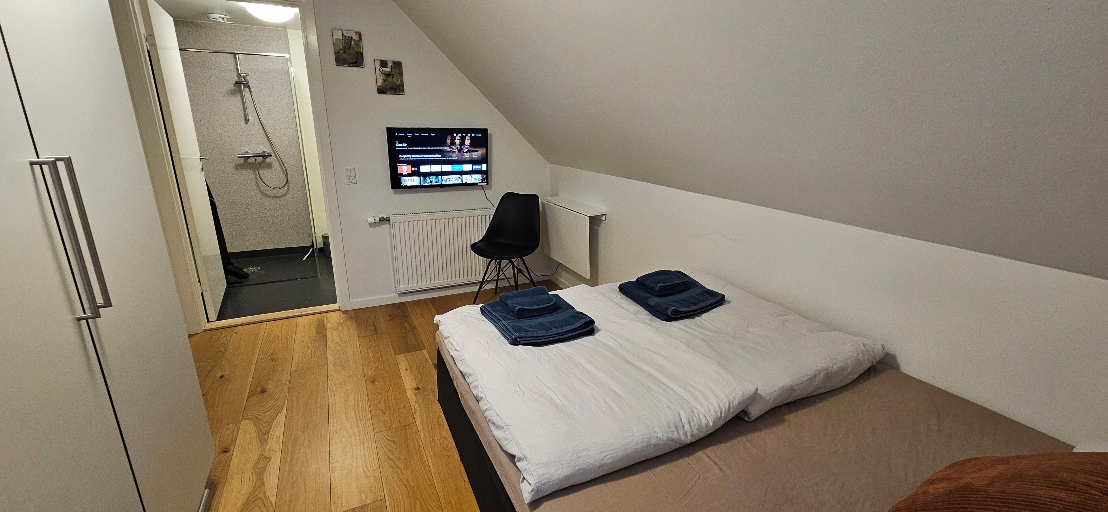 A bedroom with a bed, a chair, a TV, and a shower area.