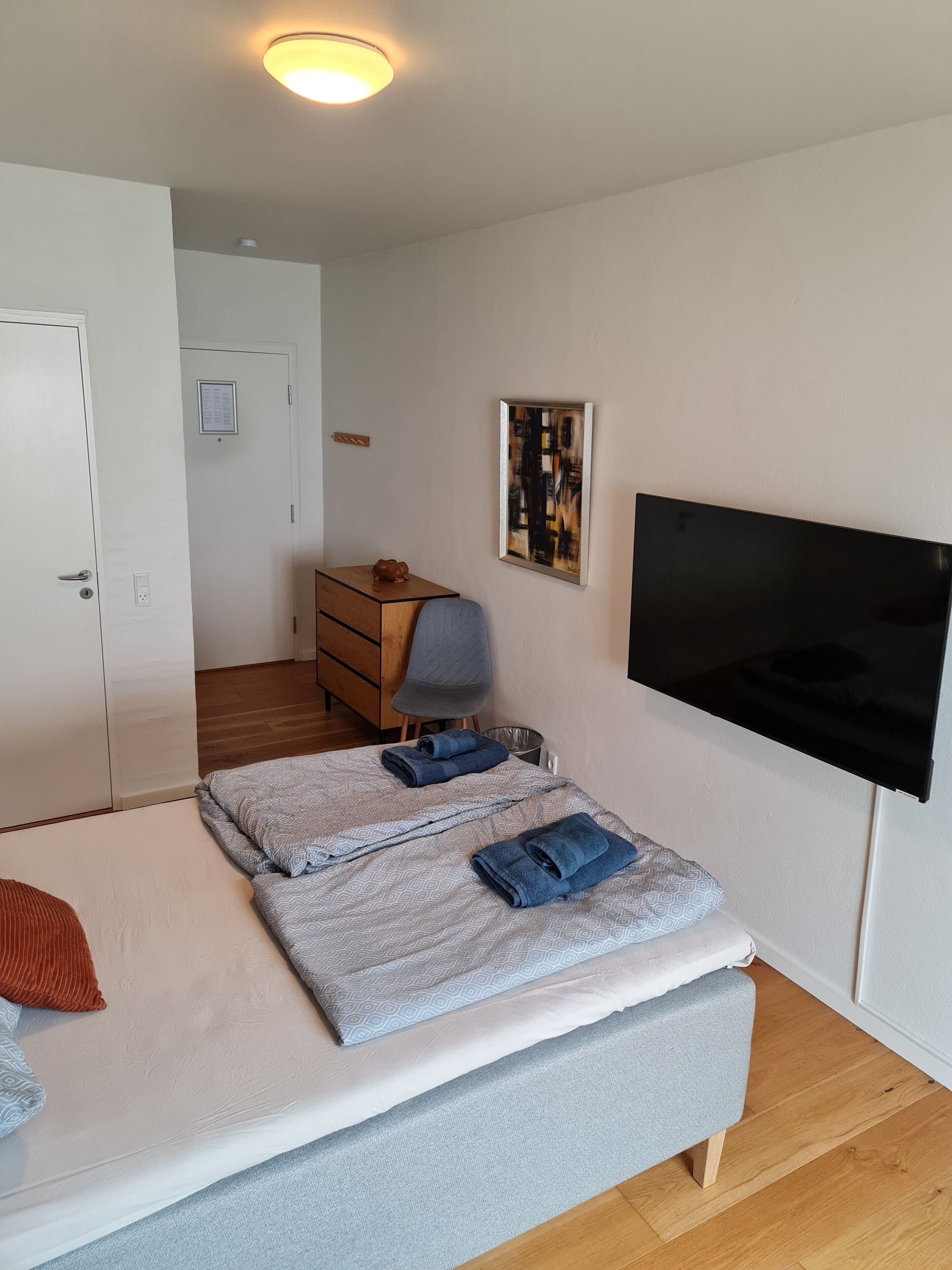 Un dormitorio con cama, escritorio, silla, televisor y puerta.