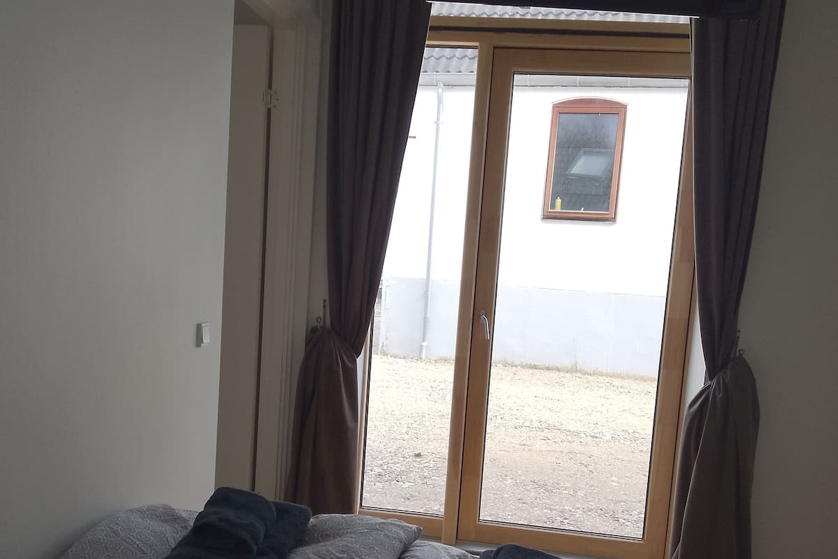 A room with a bed, a window with curtains, and a view of a building outside.