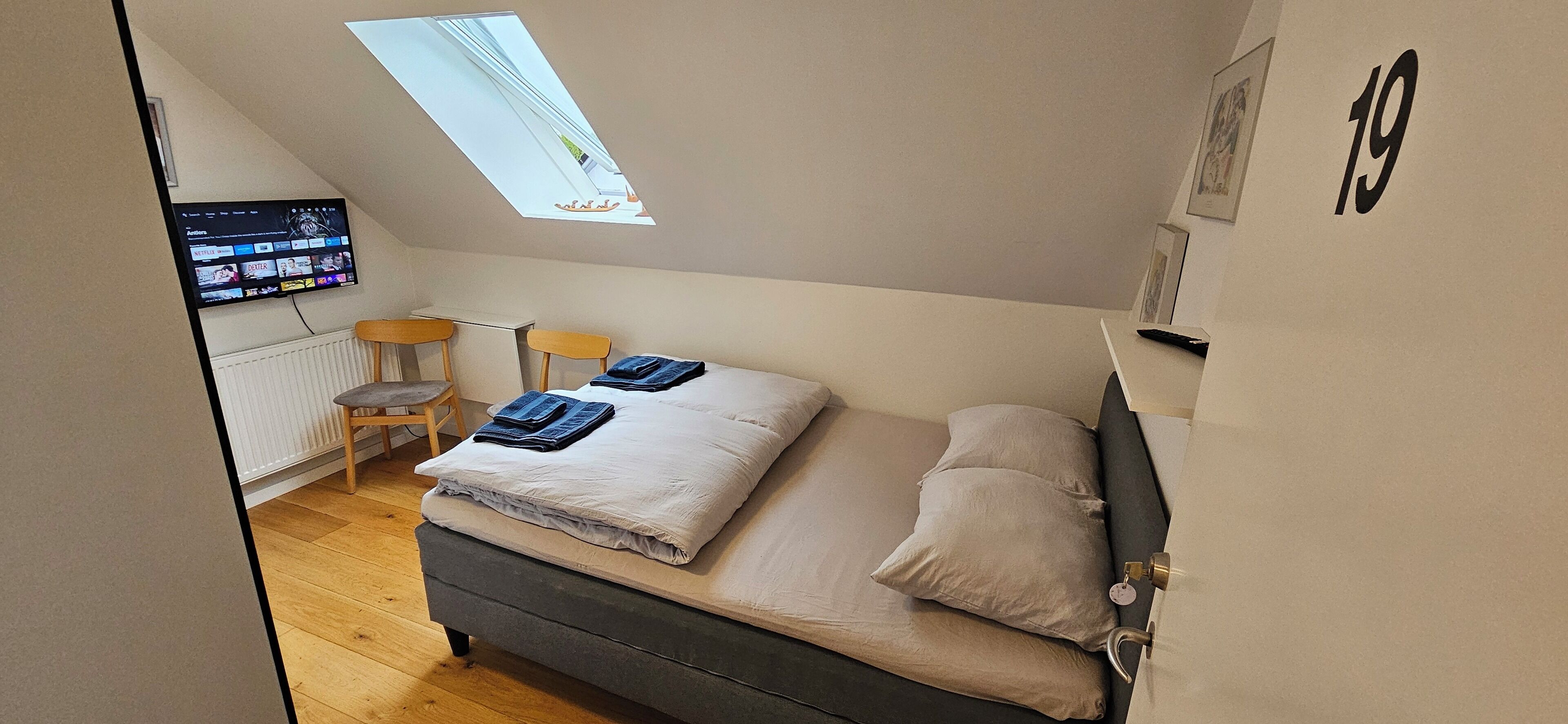 A bedroom with a bed, a desk, and a TV mounted on the wall.