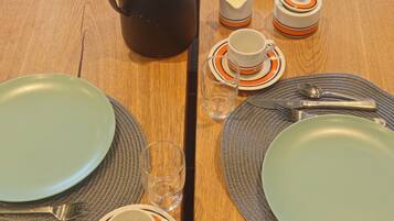 Una mesa de comedor dispuesta con platos, cubiertos, una cafetera y una cesta de pan.