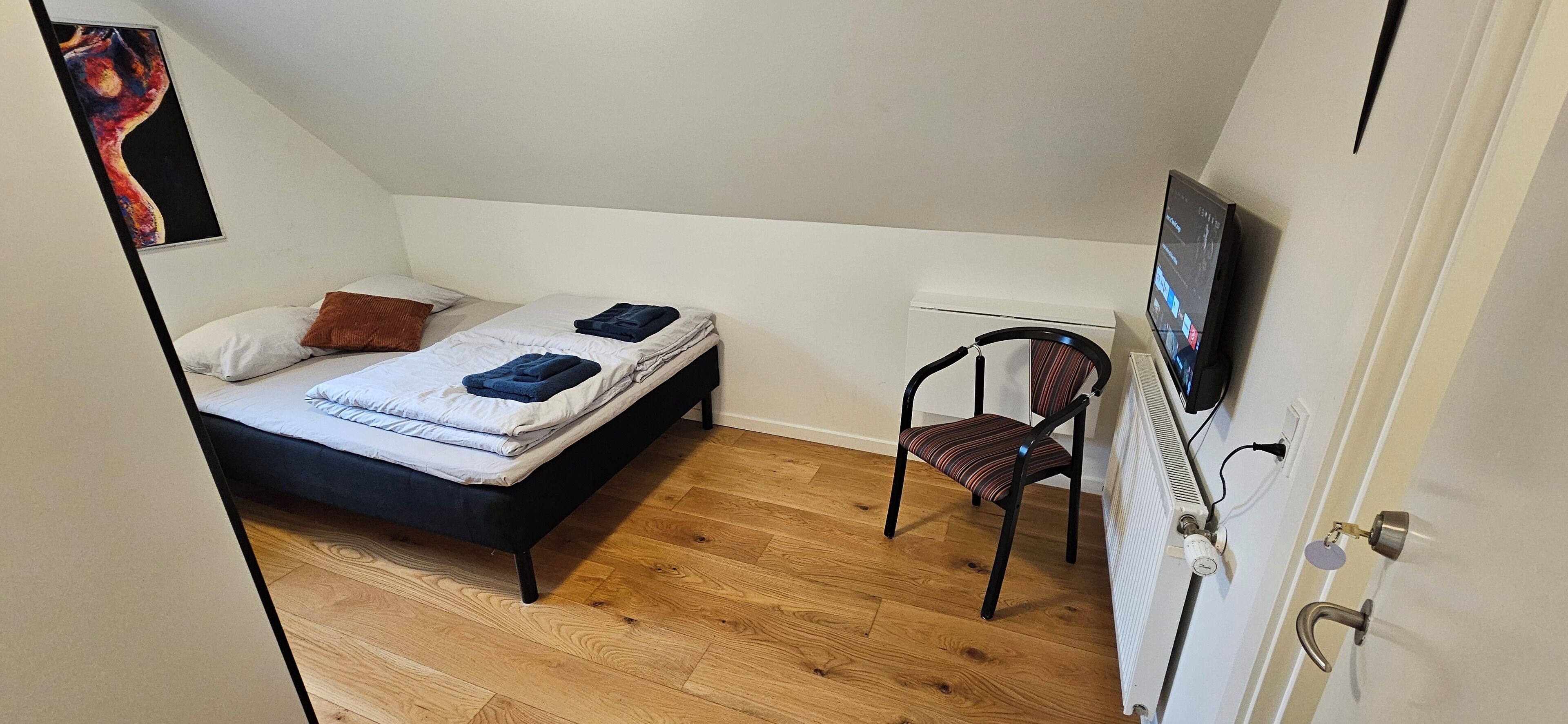 A small, tidy room with a bed, a chair, and a radiator.
