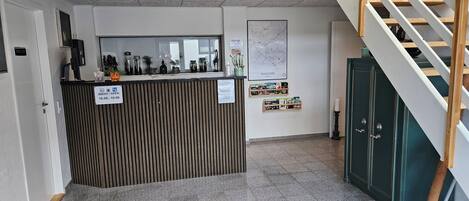 Ein Empfangsschalter mit Schild zur Angabe der Öffnungszeiten, einer Karte an der Wand und einer Treppe rechts.