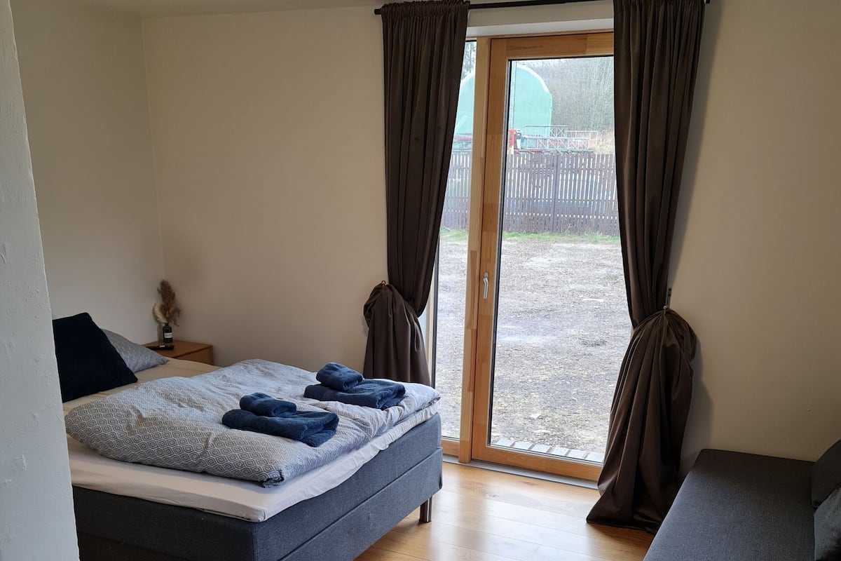 A bedroom with a bed, a sofa, a small table, and a window with curtains.
