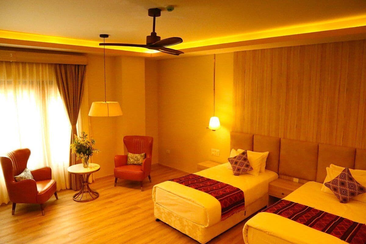 A hotel room with two beds, a sitting area with a chair and a table, and a ceiling fan.