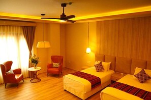 A hotel room with two beds, a sitting area with a chair and a table, and a ceiling fan. - KAACHI GRAND (Paro)
