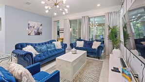 A modern living room with two blue sofas, a marble coffee table, and a large window with curtains.