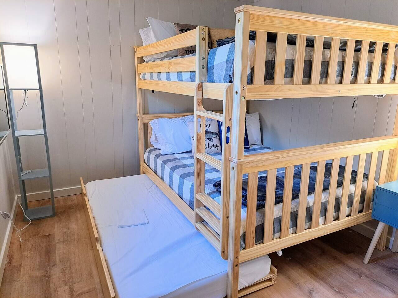 A bunk bed with a desk and a ladder in a room with wooden flooring and a white wall.