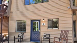 A two-story building with a blue door, two windows with shutters, and a porch with three chairs. - Two cabins in one! Family getaway near SDC & Lake! (branson)