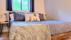 A bedroom with a bed, a nightstand, a window with curtains, and a view of trees outside. - Timber Point - Cabin on Indian Point! - Location! (Branson)