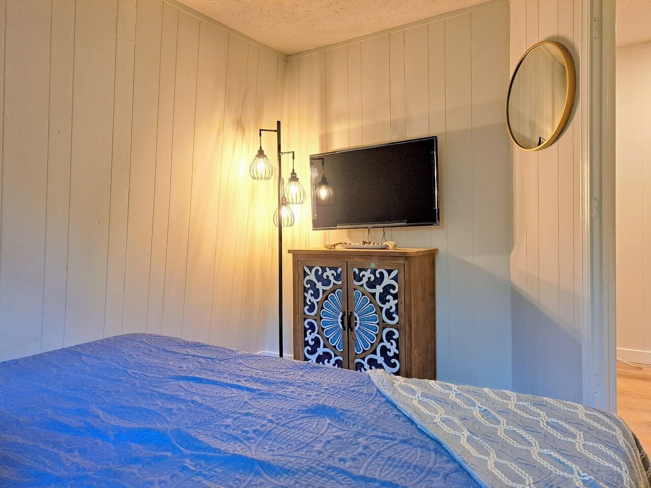 Une chambre à coucher avec un lit, un téléviseur fixé au mur et un meuble avec des portes décoratives.