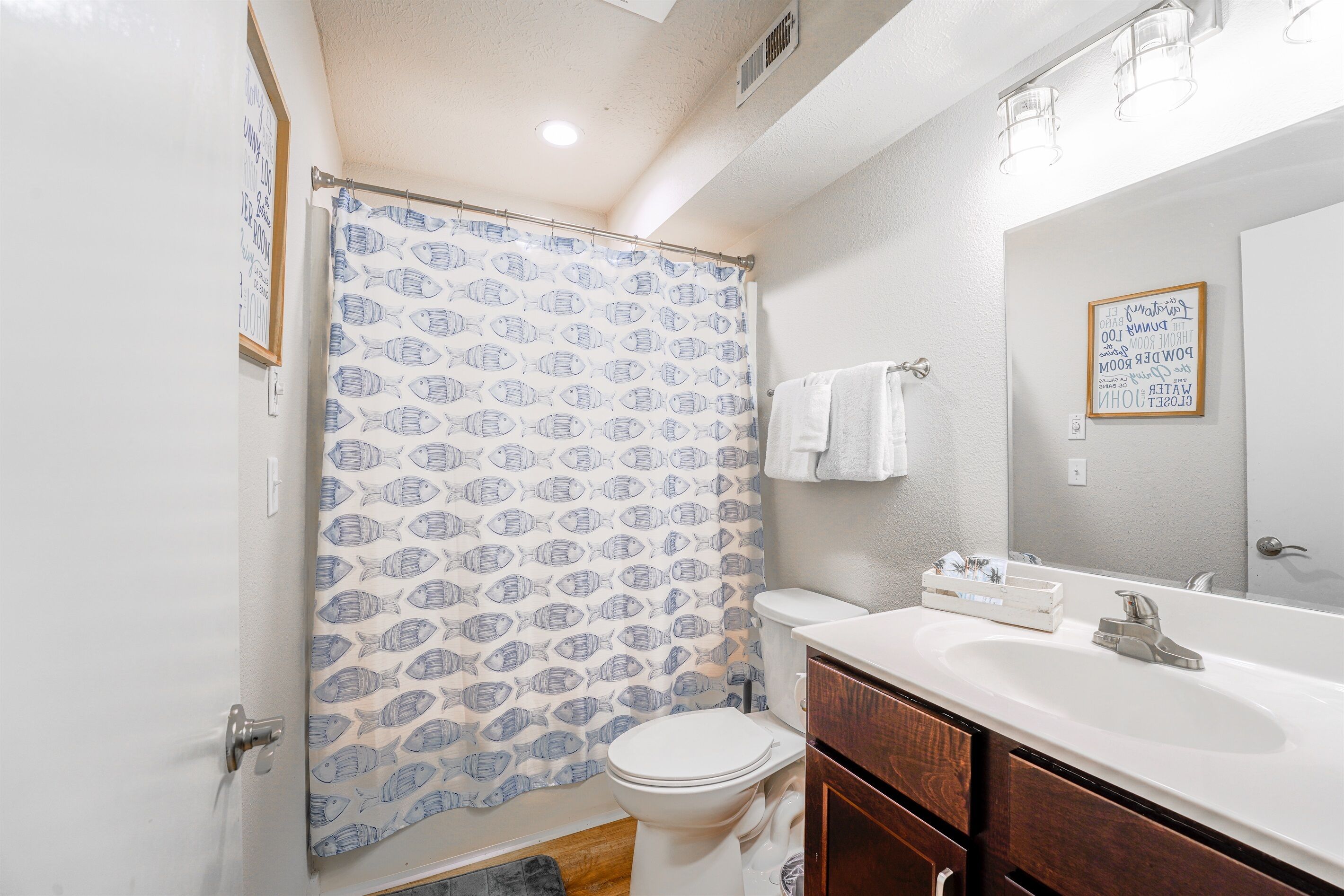 Une salle de bain équipée de toilettes, d’un lavabo et d’un rideau de douche orné d’un motif de poissons.