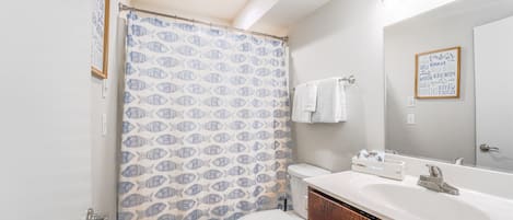 Une salle de bain équipée de toilettes, d’un lavabo et d’un rideau de douche orné d’un motif de poissons.