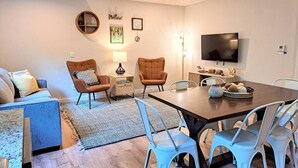A modern living room with a sofa, two armchairs, a dining table with chairs, a TV, and a fireplace. - Timber Point - Renovated Cabin on Indian Point (Branson)