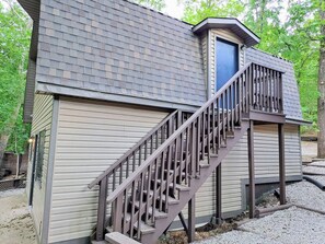 Un petit bâtiment à l’extérieur en bois, avec un escalier en métal menant à une porte.