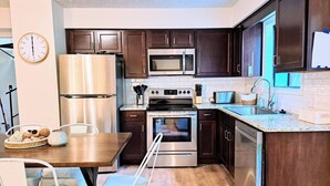 A modern kitchen with dark wooden cabinets, stainless steel appliances, a wooden dining table, and a clock on the wall. - Timber Point - Renovated Cabin on Indian Point (Branson)